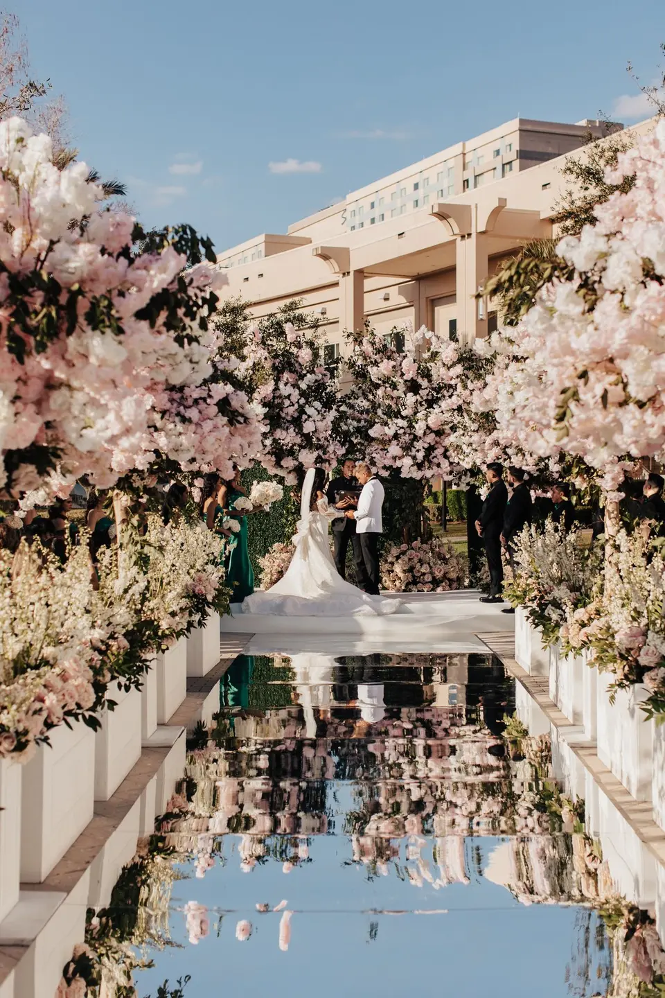 A lavish outdoor wedding ceremony surrounded by abundant blush florals and a mirrored aisle