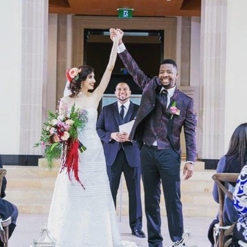 Newlyweds raising their joined hands as Pastor Wayde celebrates behind them