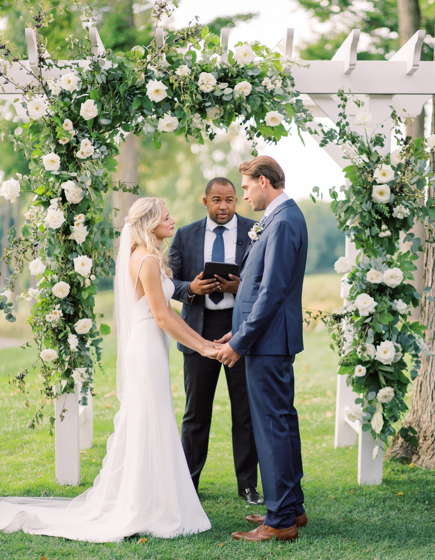 Wayde officiating a wedding beneath an abundant floral arch