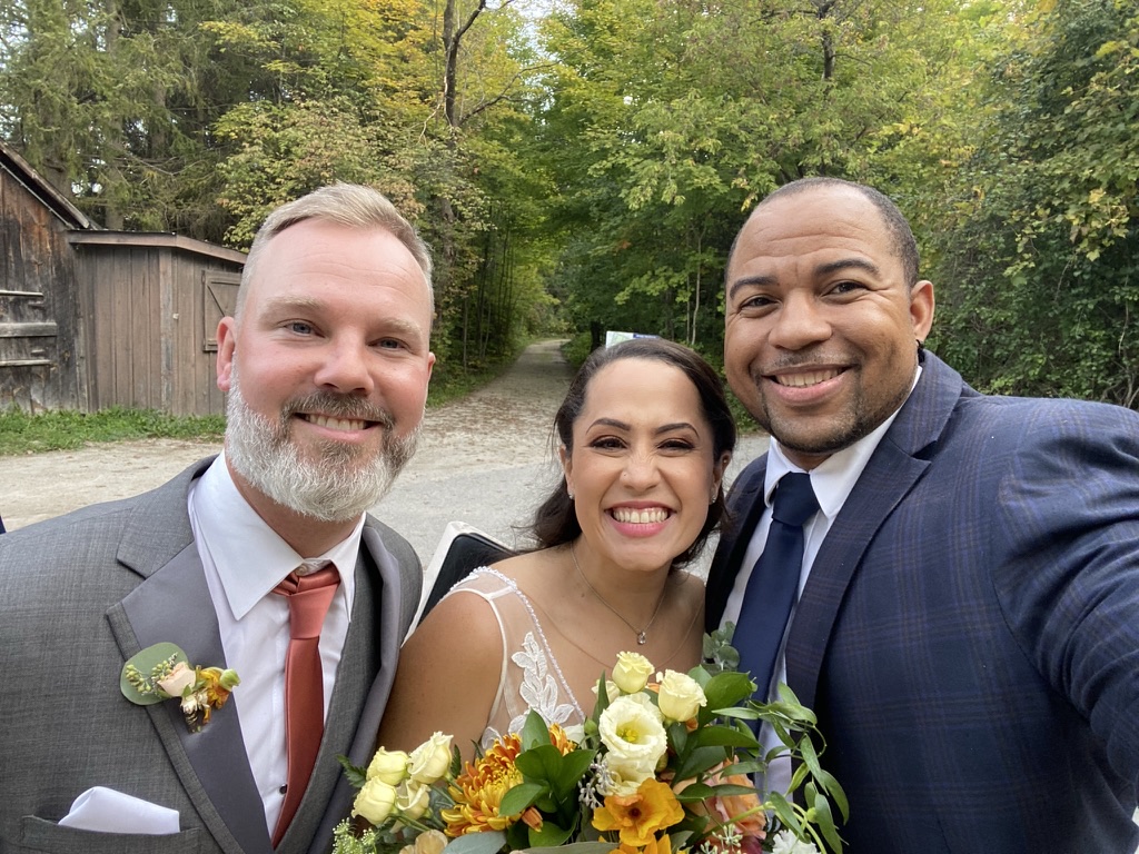 Wayde and newlyweds smiling beside an autumn bouquet