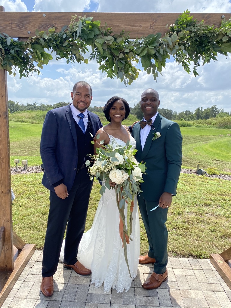 Wayde with newlyweds beneath a wooden ceremony arbor